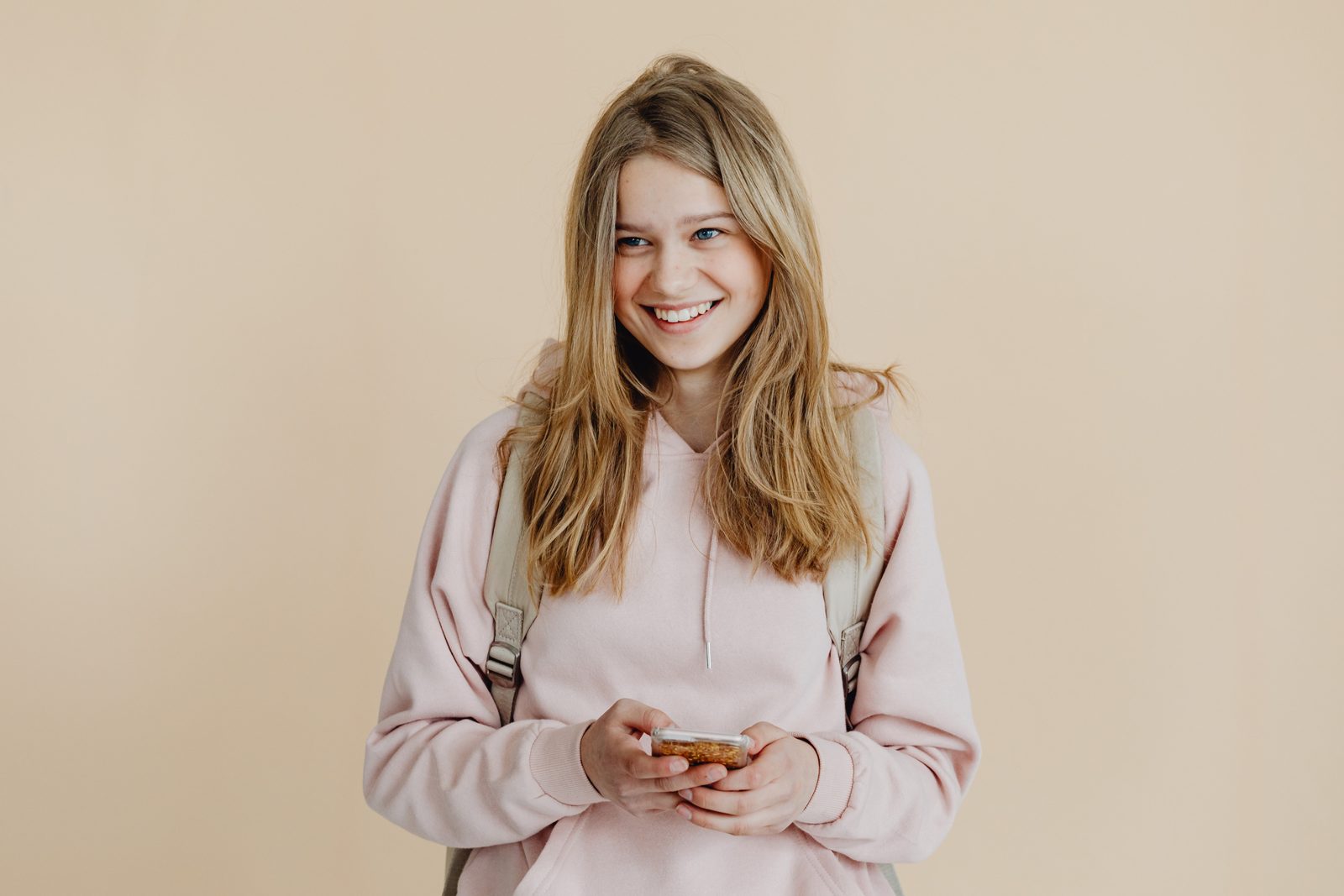 Smiling teenage girl with a backpack holding her phone