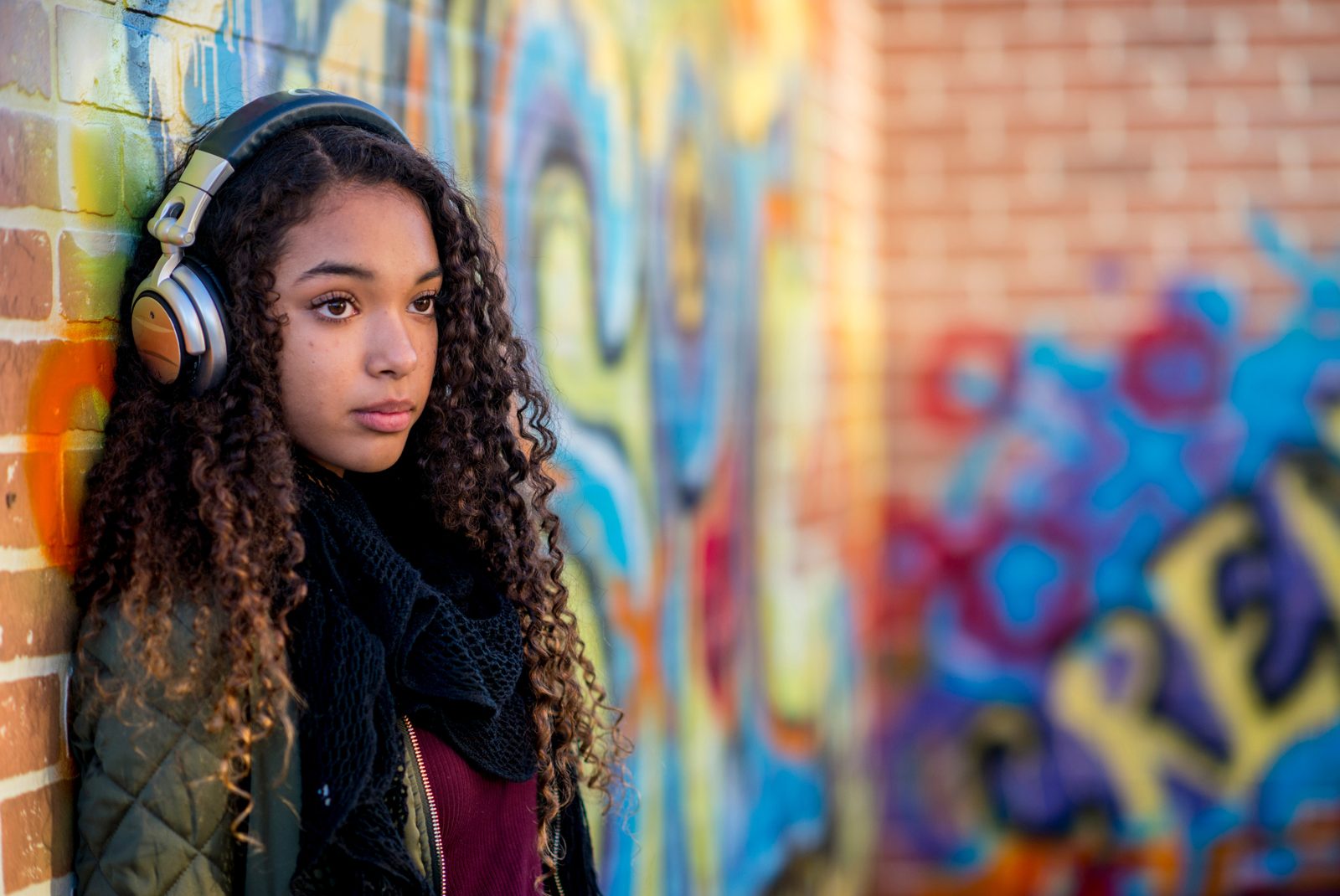Teenager with headphones leaning against a colourful graffiti wall